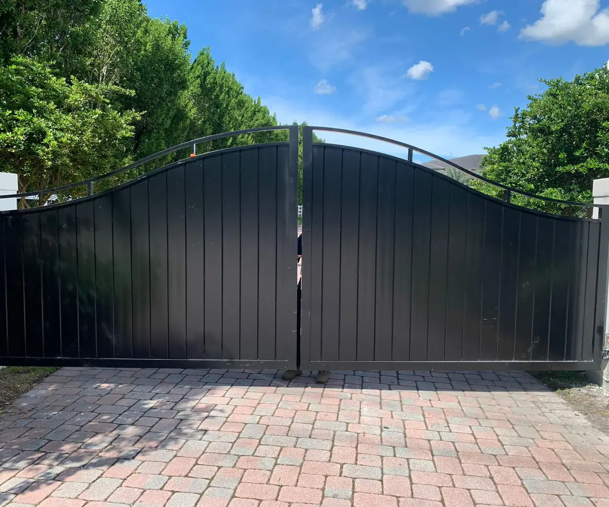 Black arched aluminum driveway gate over brick pavers